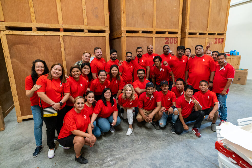 Group photo of the entire Santa Fe Relocation Services team wearing red uniforms, gathered in a warehouse setting, showcasing their unity and dedication to providing moving and relocation services.