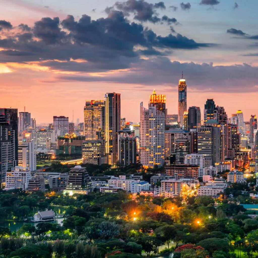 A breathtaking view of the Bangkok skyline at sunset, showcasing towering skyscrapers and lush green spaces. Santa Fe Relocation provides expert moving services to help you relocate seamlessly to global cities like Bangkok.