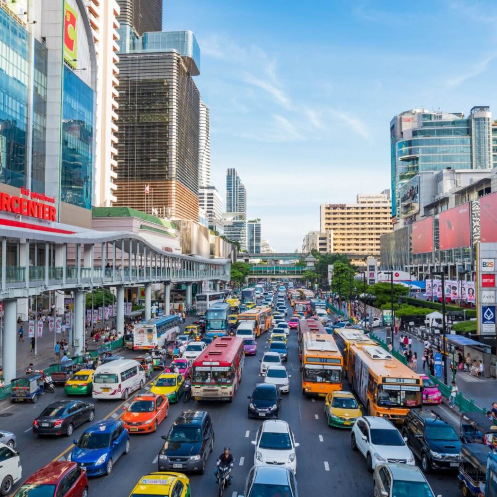 A bustling city street in Bangkok, Thailand, filled with colorful taxis, buses, and modern shopping centers. Santa Fe Relocation helps businesses and individuals navigate the transition to life in vibrant urban destinations like Bangkok.